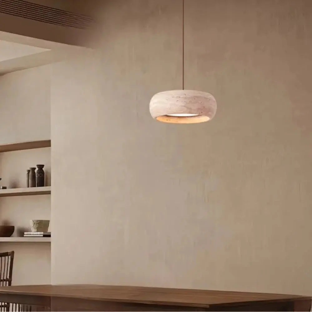 Suspension en travertin suspendue au-dessus d’une table en bois dans un intérieur minimaliste aux tons chauds.