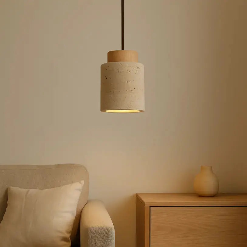 Suspension en travertin éclairée dans un salon au style scandinave, avec un fauteuil beige et un meuble en bois clair en arrière-plan.