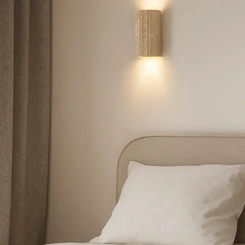 Applique murale en travertin Lunda éclairée dans une chambre minimaliste au style scandinave, lumière douce vers le haut et le bas.