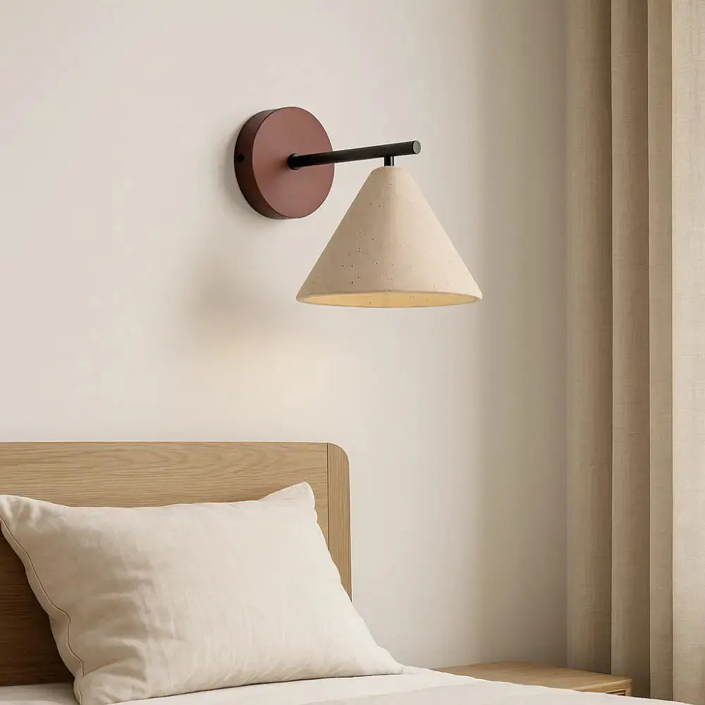 Applique murale en travertin Lyra éclairant une chambre minimaliste avec tête de lit en bois clair et rideaux beiges.
