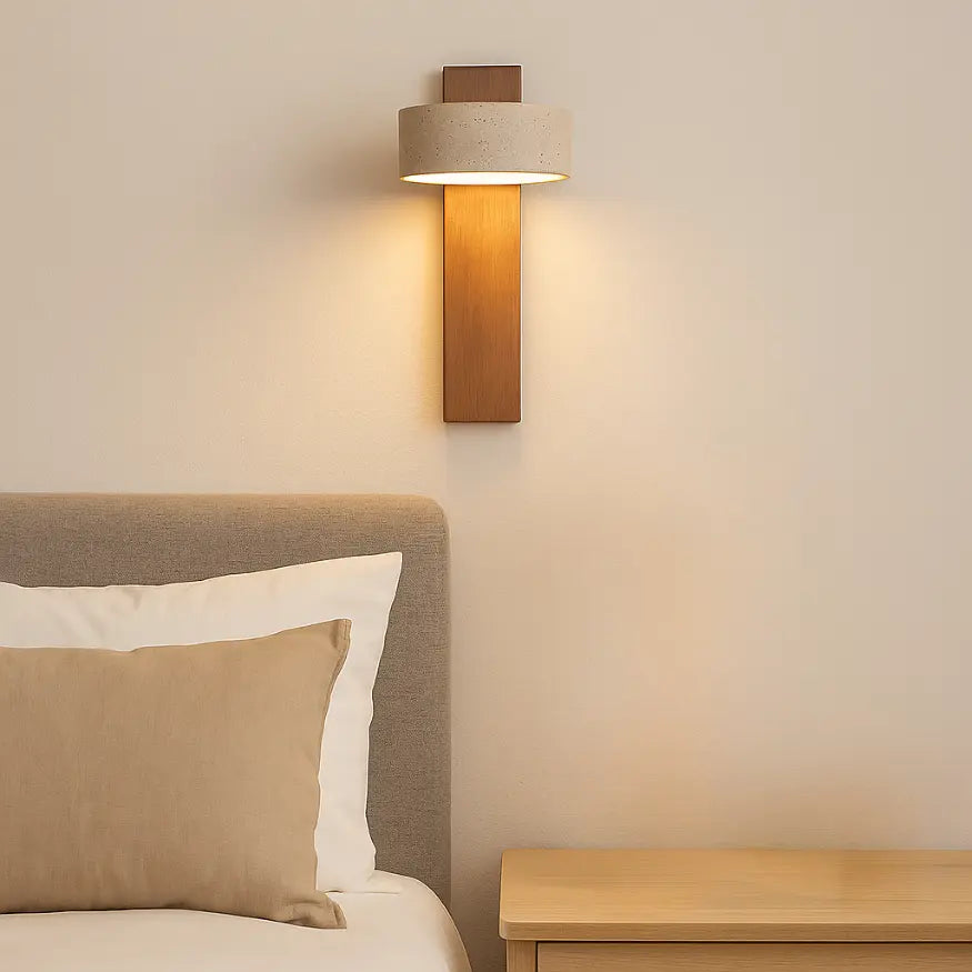 Applique murale Solberg en travertin naturel et bois, diffusant une lumière douce au-dessus d’un lit dans une chambre épurée. 