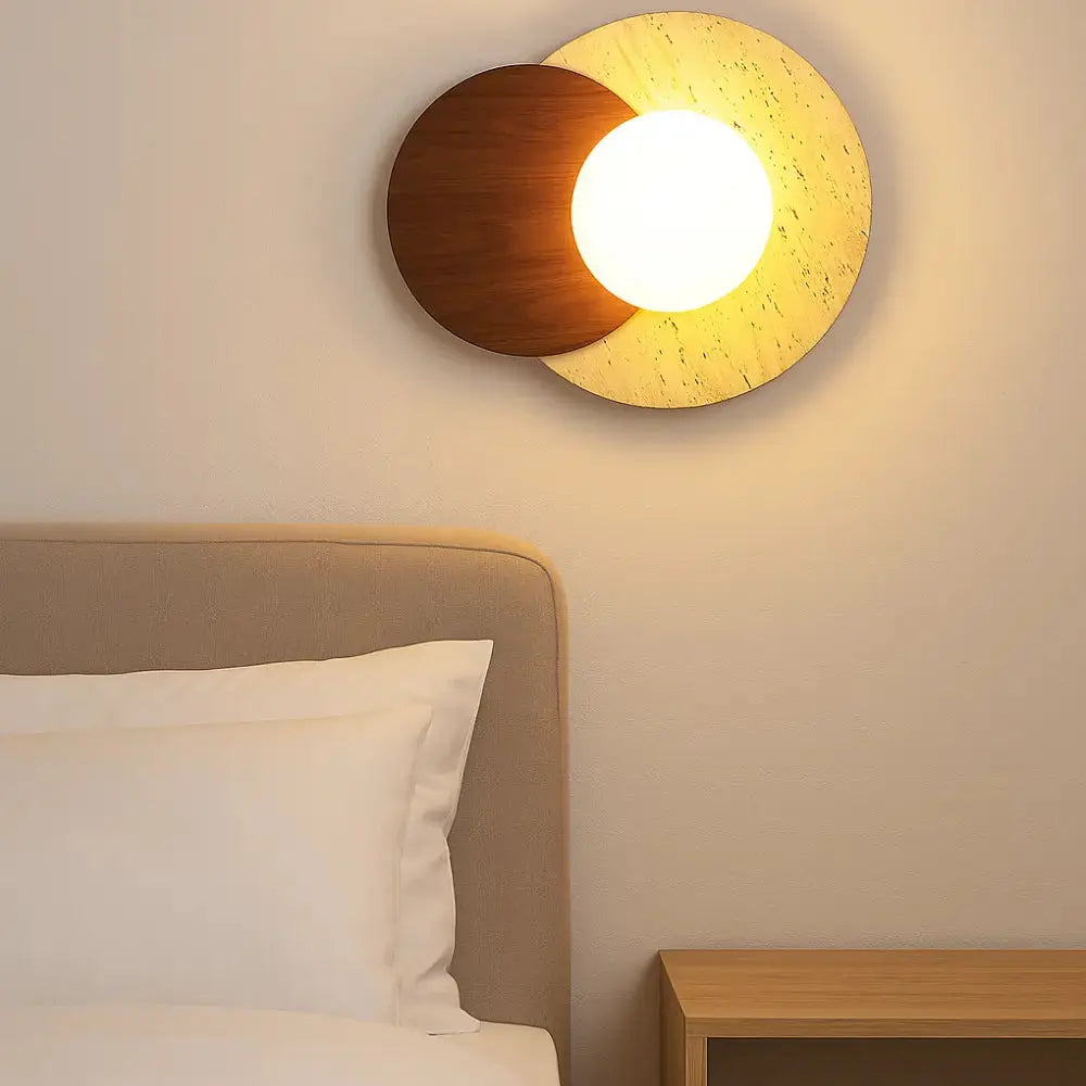 Applique murale en travertin et bois allumée au-dessus d’un lit, design circulaire sculptural Verdalsøra en style nordique.