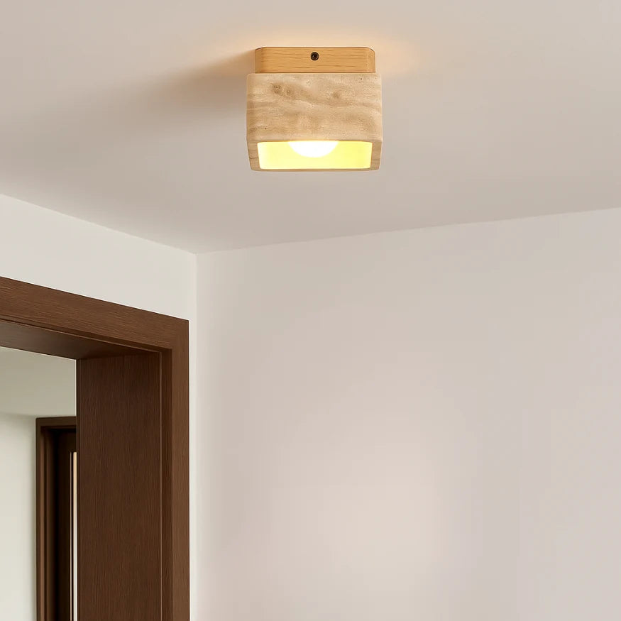 Plafonnier cubique en travertin et bois massif, diffusant une lumière chaude, installé dans un intérieur moderne aux lignes épurées. 