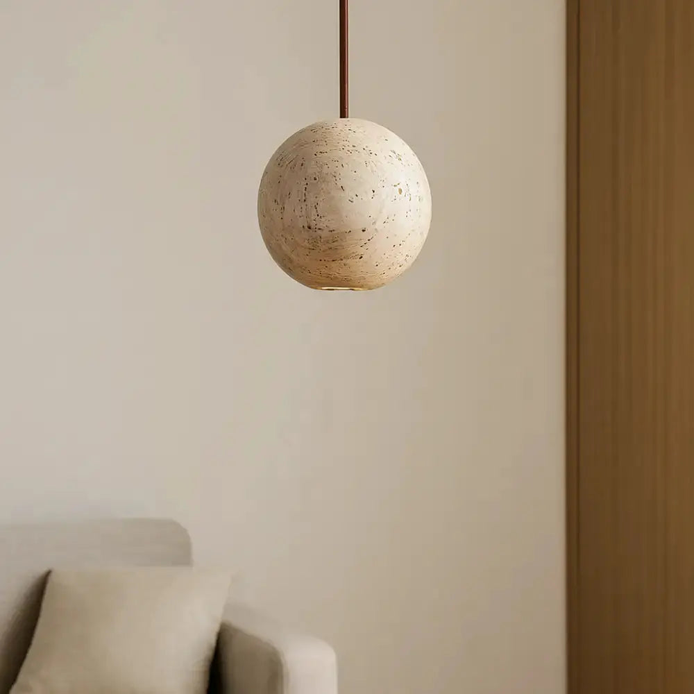 Suspension sphérique en travertin suspendue au-dessus d’un espace salon minimaliste beige, design scandinave naturel. 